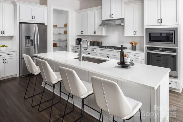 a kitchen with stainless steel appliances a dining table chairs a refrigerator and cabinets