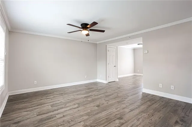a view of an empty room with wooden floor and a ceiling fan