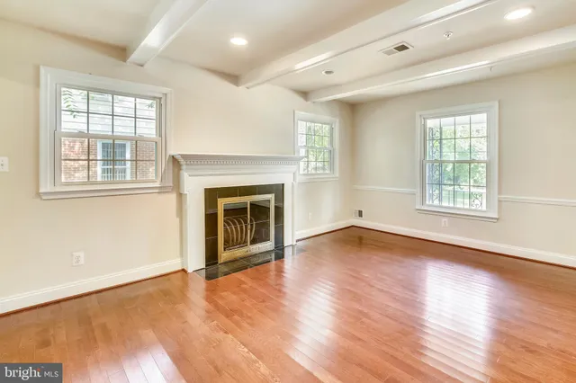 an empty room with wooden floor fireplace and windows