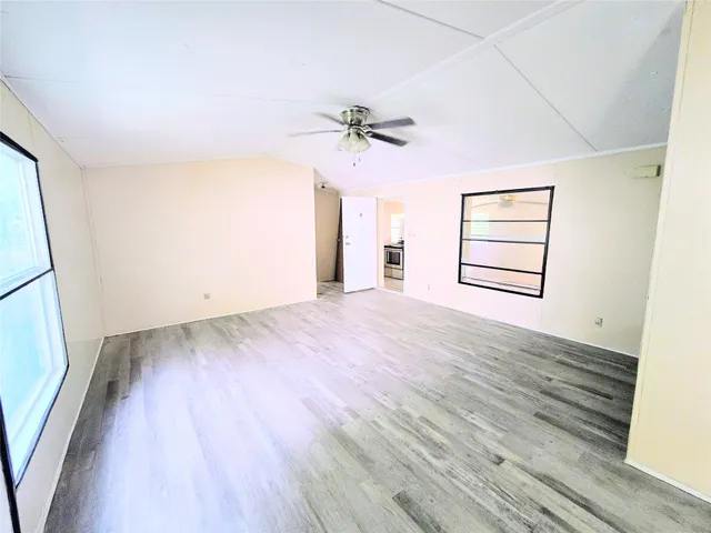 an empty room with wooden floor ceiling fan and windows