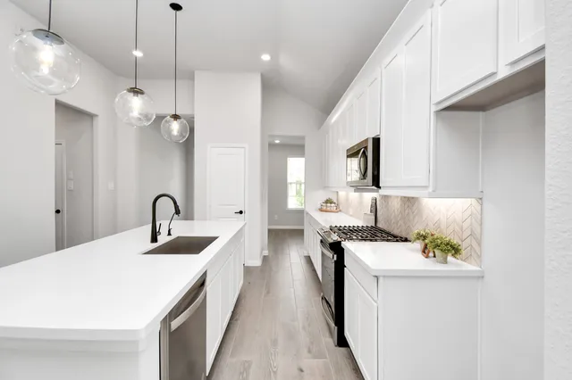 a large white kitchen with stainless steel appliances kitchen island a stove a sink a center island and living room view