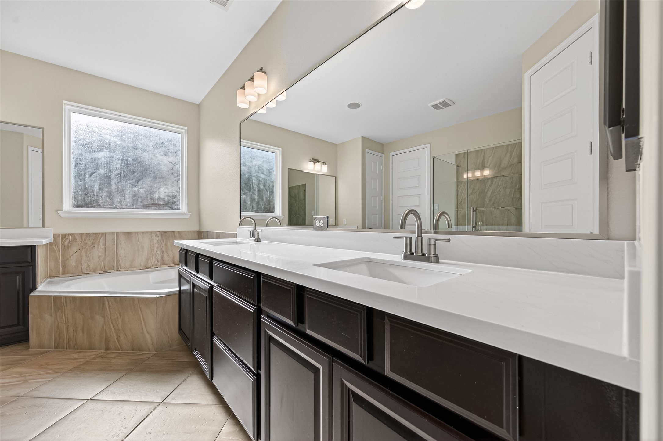 7003 Bristol Memorial Drive Spring, TX 77379 - Photo 23 of 40 Alternate view of the primary bathroom in this Spring TX 77379 home highlighting the spacious layout and seamless flow between the soaking tub and dual-sink vanity. Dark cabinetry contrasts with light countertops and tile flooring for a clean, modern finish. Generous counter space and storage enhance functionality, while the open design complements the private primary suite in this move-in ready home near The Woodlands.