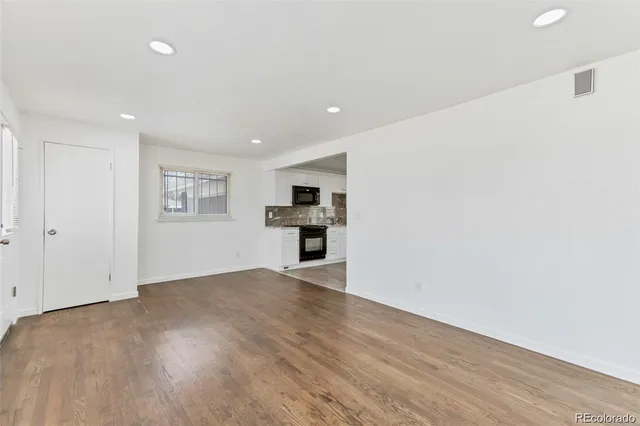 a view of empty room with wooden floor and kitchen