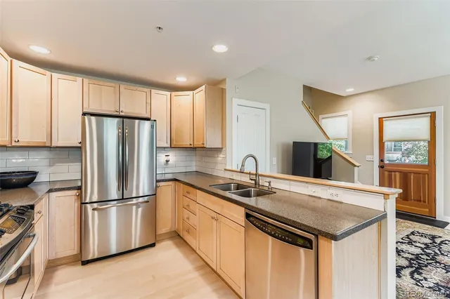 a kitchen with stainless steel appliances granite countertop a refrigerator a sink a stove and white cabinets with wooden floor