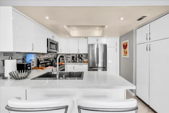 a living room with stainless steel appliances lots of white furniture and a refrigerator