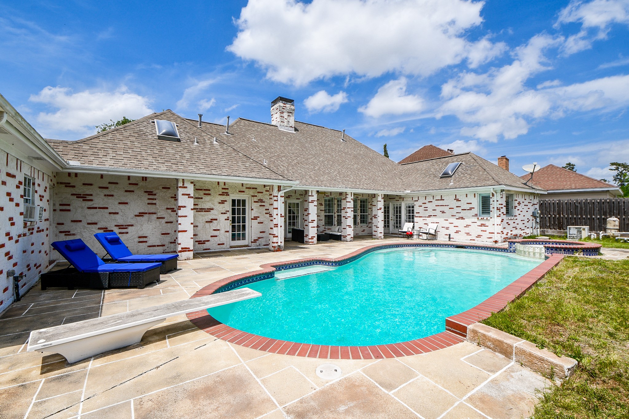 263 Wood Loop Street Houston, TX 77015 - Photo 13 of 45 This photo showcases a charming home exterior with a spacious backyard featuring a large, inviting swimming pool. The patio area includes comfortable lounge chairs, perfect for relaxation. The house has a unique brick design and ample windows, providing a bright and airy atmosphere.