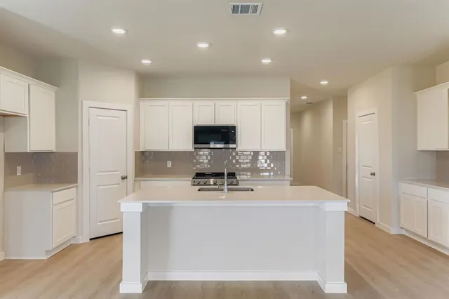 a view of a kitchen with kitchen island a sink dishwasher stove with wooden floor and cabinets