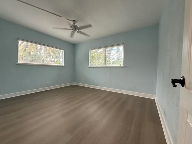 an empty room with wooden floor fan and windows