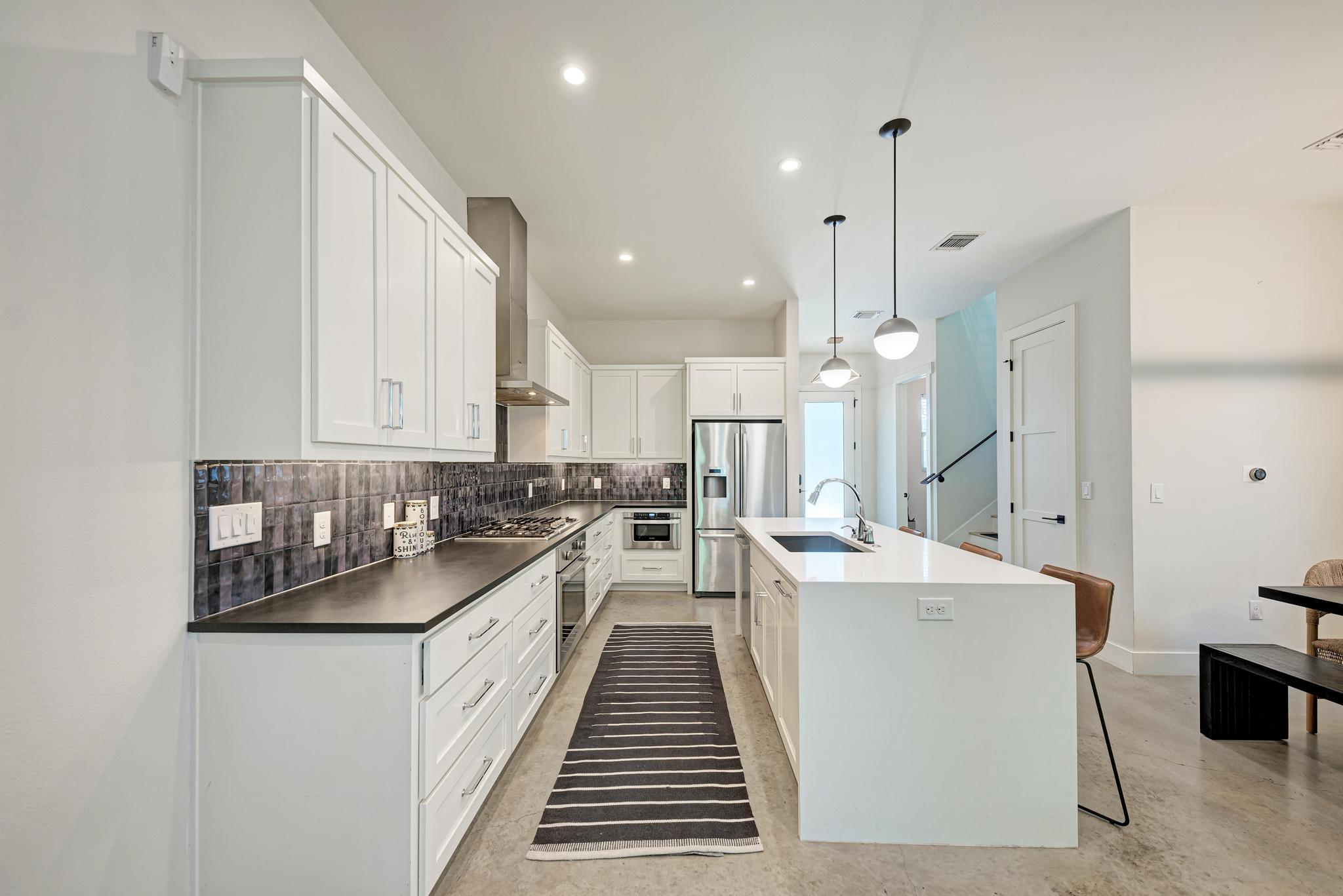 918 Cardinal Lane, Unit A Austin, TX 78704 - Photo 9 of 40 The kitchen steals attention in all the right ways with under-lit custom cabinetry, statement pendants, premium stone surfaces, and designer tile backsplash.