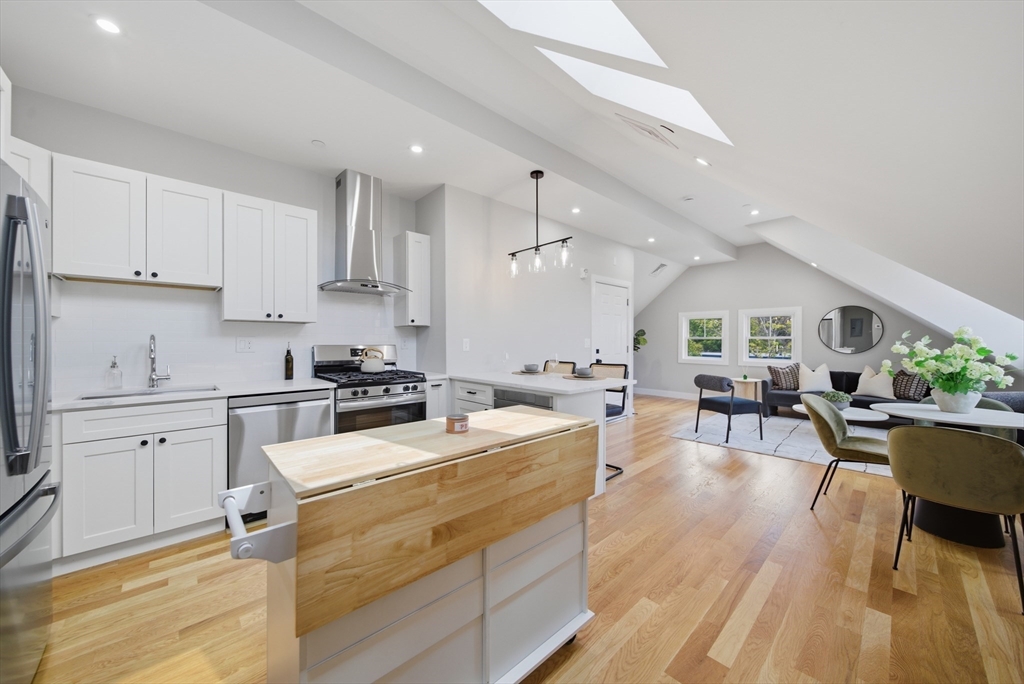 174 Walnut Street, Unit 3 Somerville, MA 02145 - Photo 28 of 38 a open kitchen with stainless steel appliances kitchen island granite countertop a stove a sink a dining table and chairs with wooden floor