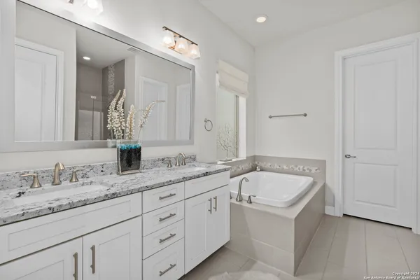 a bathroom with a granite countertop double vanity sink and mirror with bathtub