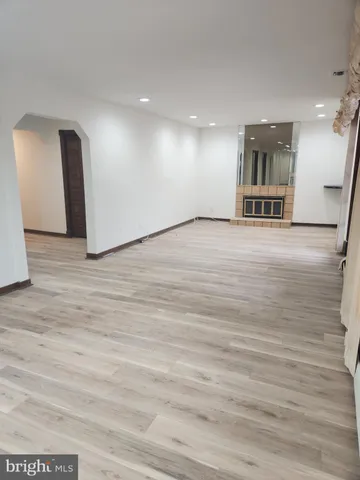 a view of an empty room with wooden floor and kitchen view