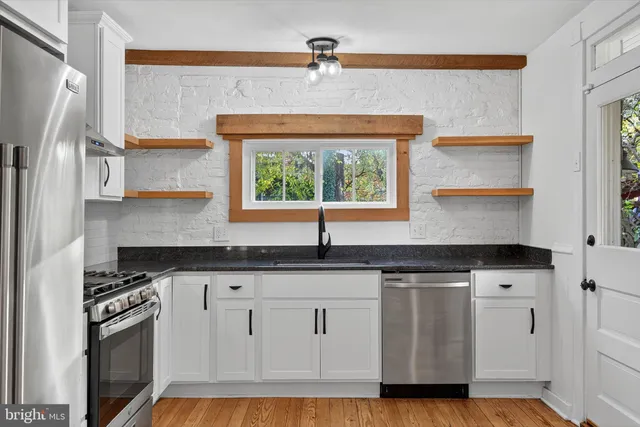 a kitchen with granite countertop a sink cabinets stainless steel appliances and a window