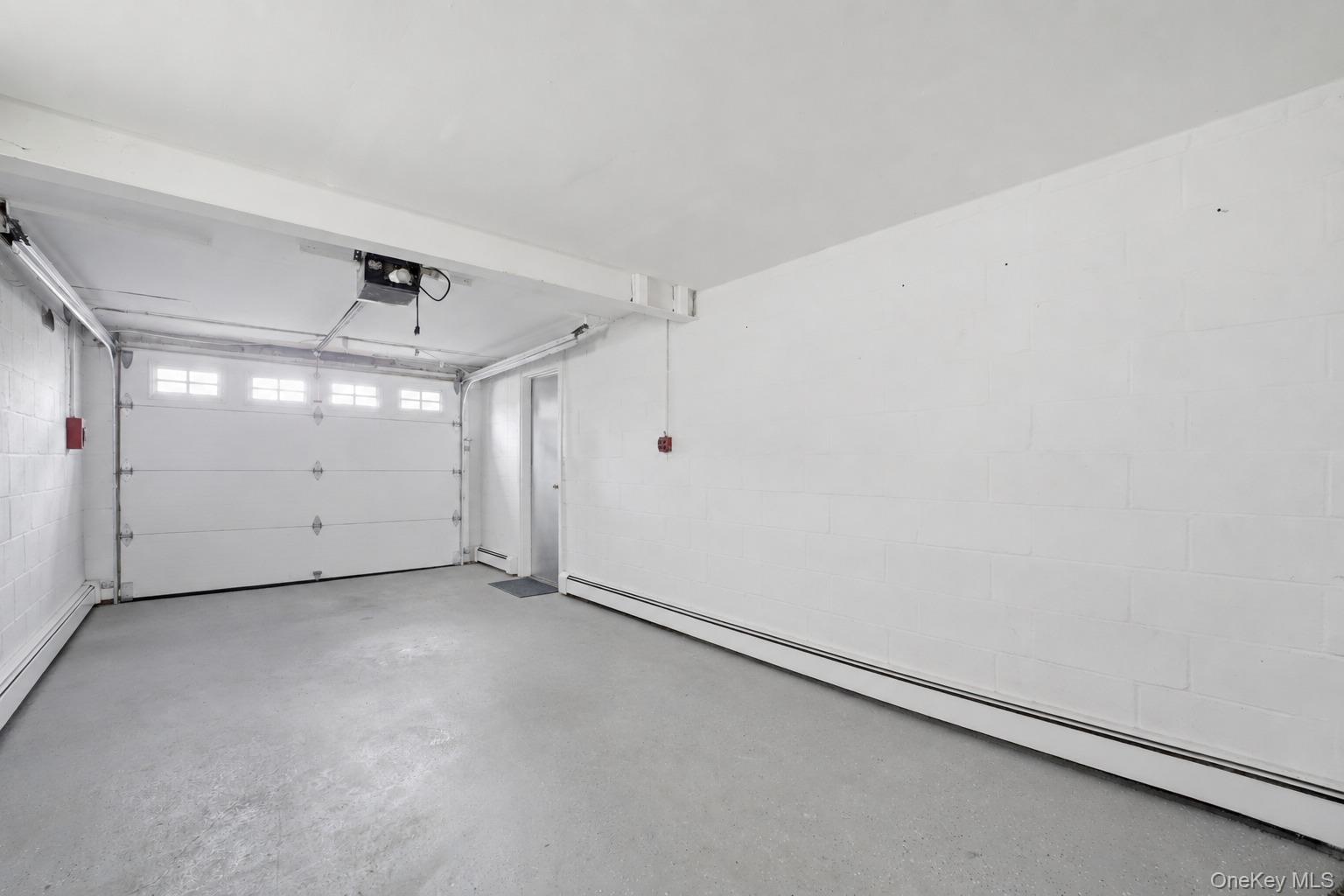 144 Bell Road Scarsdale, NY 10583 - Photo 38 of 49 Attached garage space featuring a paneled garage door with upper window inserts, an automatic opener, concrete flooring, and painted cinder block walls