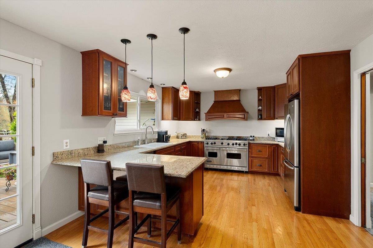 2540 Muir Court Cool, CA 95614 - Photo 22 of 97 kitchen featuring appliances with stainless steel finishes, hanging light fixtures, light wood-type flooring, a kitchen bar, and custom range hood