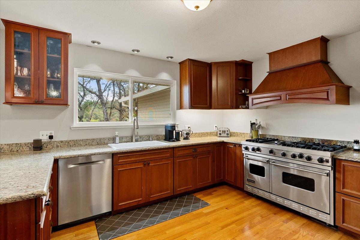 2540 Muir Court Cool, CA 95614 - Photo 23 of 97 kitchen featuring appliances with stainless steel finishes, light wood-style flooring, premium range hood, light stone countertops, and glass insert cabinets