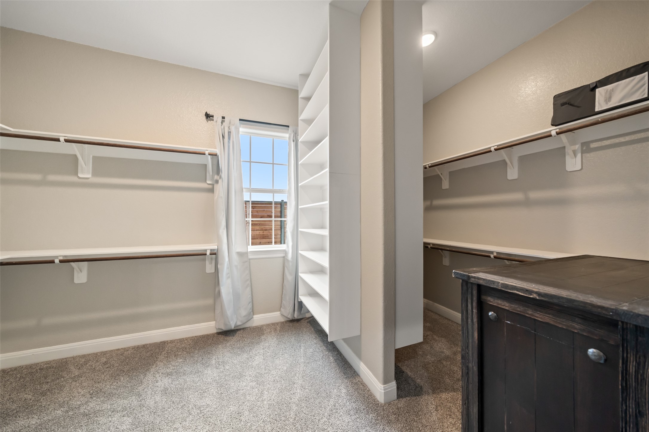 10630 Padon Road Needville, TX 77461 - Photo 26 of 50 Walk-in primary closet offers built-in shelving, dual hanging rods, and a center storage tower. Natural light from the window enhances visibility and organization.