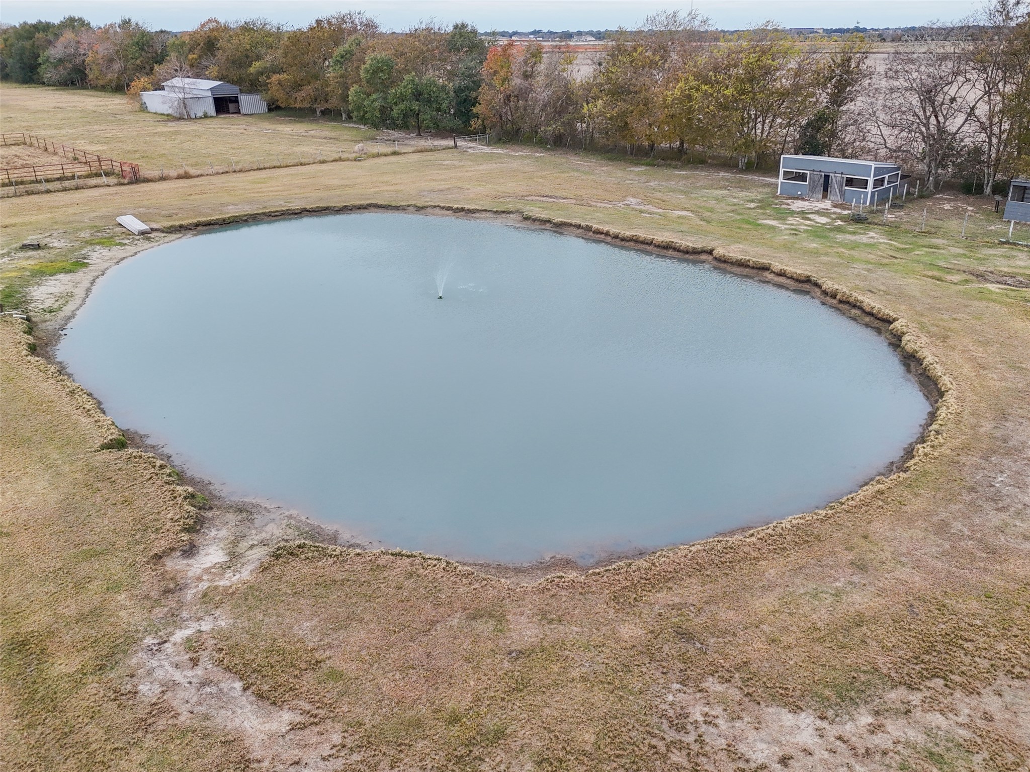 10630 Padon Road Needville, TX 77461 - Photo 36 of 50 Aerial view of the stocked pond featuring an active fountain and gently sloped banks. Open pasture surrounds the water feature, offering both function and visual appeal.