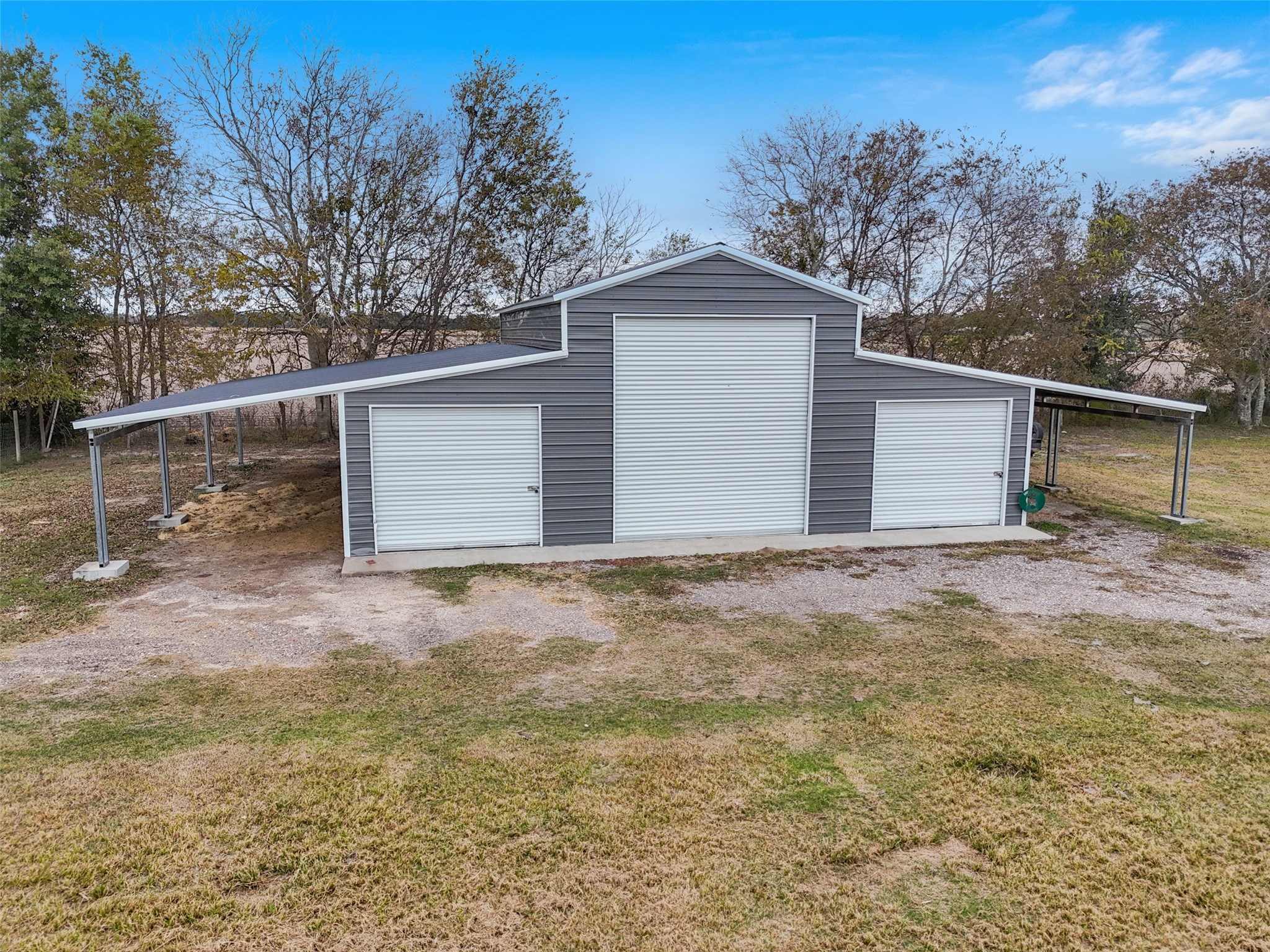 10630 Padon Road Needville, TX 77461 - Photo 37 of 50 Large metal shop with three roll-up doors and extended covered bays on both sides. Concrete foundation and wide access support equipment storage and workspace use.