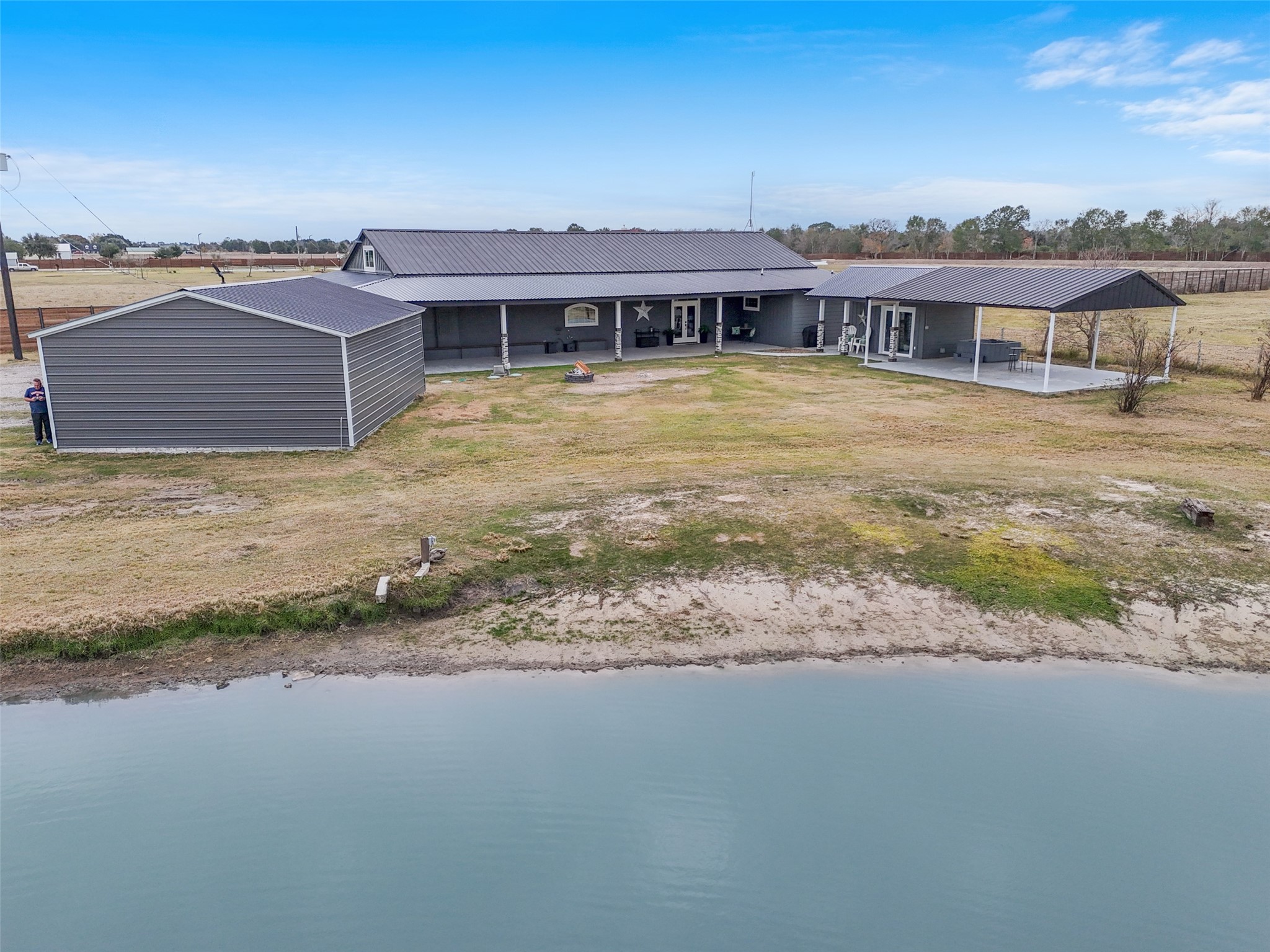 10630 Padon Road Needville, TX 77461 - Photo 48 of 50 Aerial view of the main residence shows the long covered porch, adjacent garage structure, and detached covered patio area. The pond sits directly in front of the home, enhancing the setting.