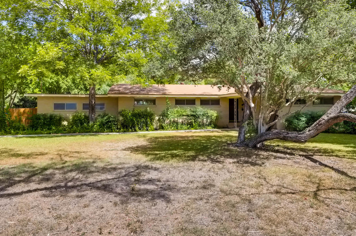 Mature trees canopy this classic brick ranch, creating a shaded retreat.