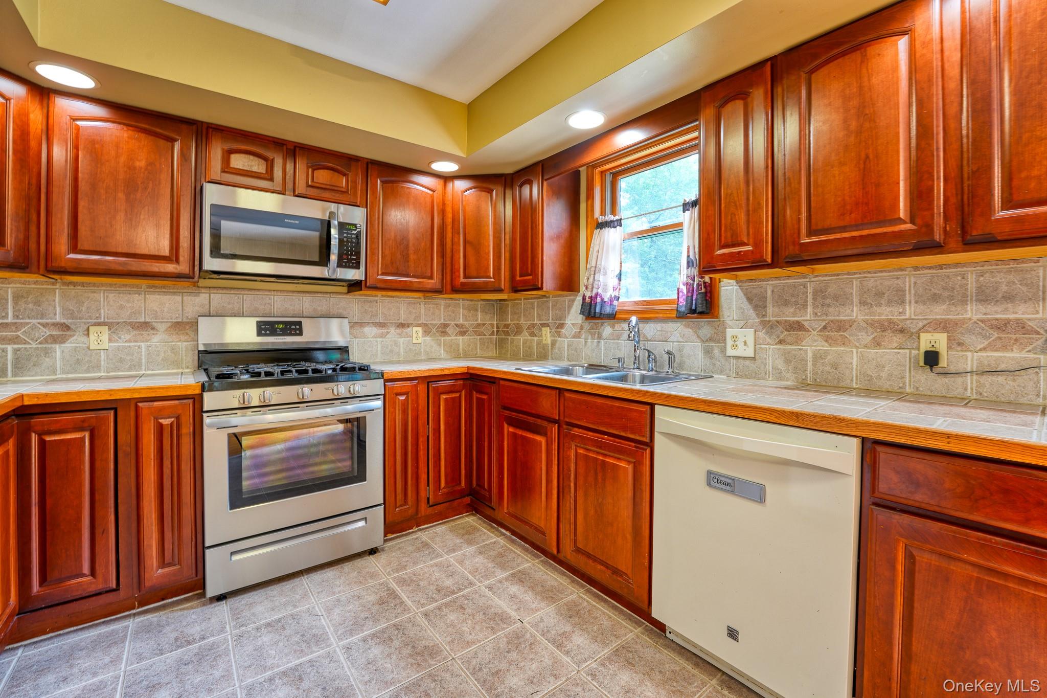 160 Barryville - Yulan Road Barryville, NY 12719 - Photo 4 of 38 Kitchen featuring appliances with stainless steel finishes, decorative backsplash, tile countertops, light tile patterned floors, and brown cabinets