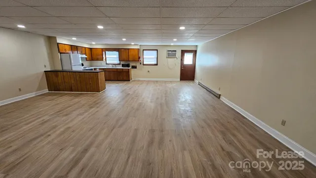 an empty room with wooden floor kitchen view and a window