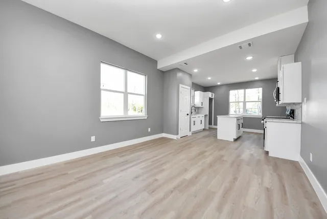 a view of an empty room with kitchen and window