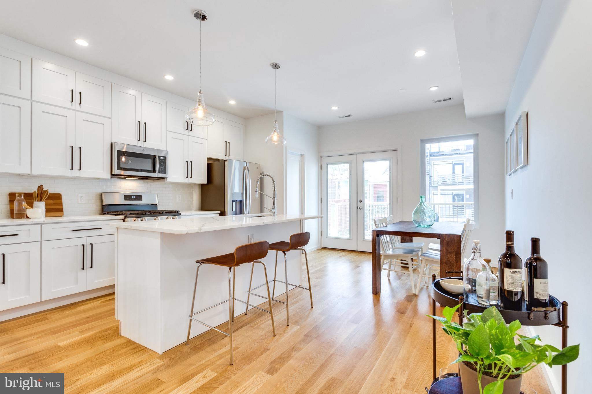 53 R Street Northeast, Unit 2 Washington, DC 20002 - Photo 2 of 25 a kitchen with stainless steel appliances granite countertop a stove top oven a sink a dining table and chairs with wooden floor