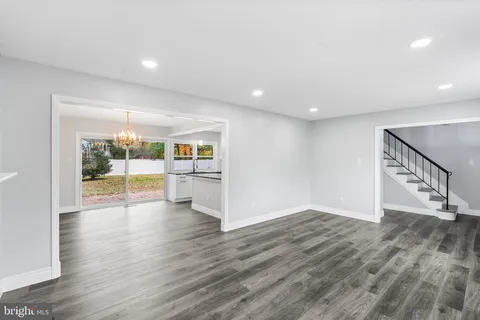 a view of an empty room with wooden floor and a kitchen