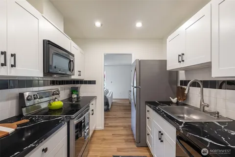 a kitchen with granite countertop a refrigerator a stove a sink and white cabinets with wooden floor