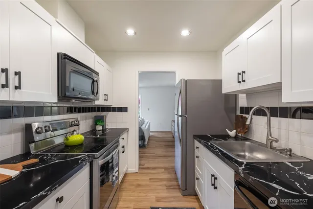 a kitchen with granite countertop a refrigerator a stove a sink and white cabinets with wooden floor