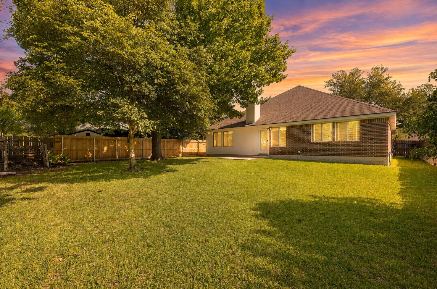 1102 Nelson Ranch Road Cedar Park, TX 78613 - Photo 35 of 37 A spacious backyard with mature trees, a wooden fence, and a brick exterior home under a beautiful sunset.