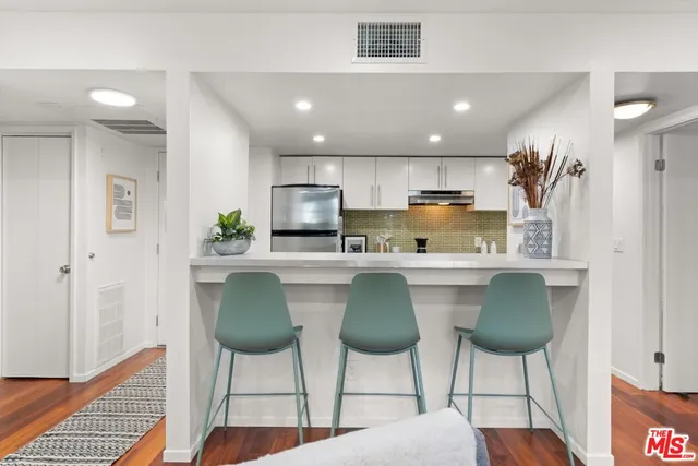 a kitchen with stainless steel appliances granite countertop a refrigerator a stove a sink dishwasher and white cabinets with wooden floor