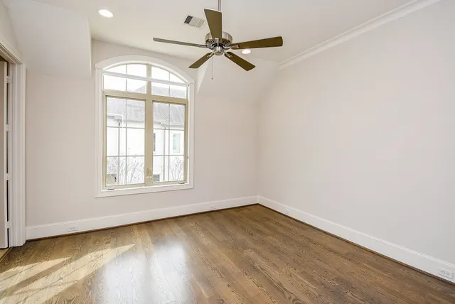 an empty room with wooden floor fan and windows