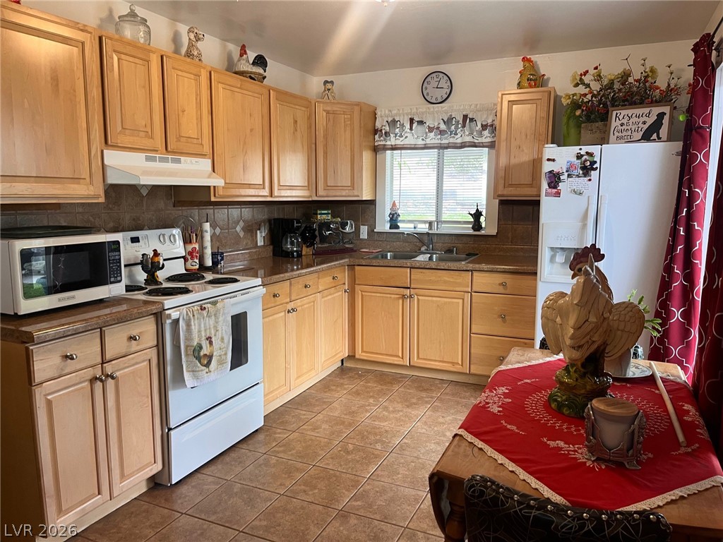 12 Reno Road Ely, NV 89301 - Photo 5 of 21 Kitchen featuring white appliances, under cabinet range hood, backsplash, light tile patterned floors, and light brown cabinets