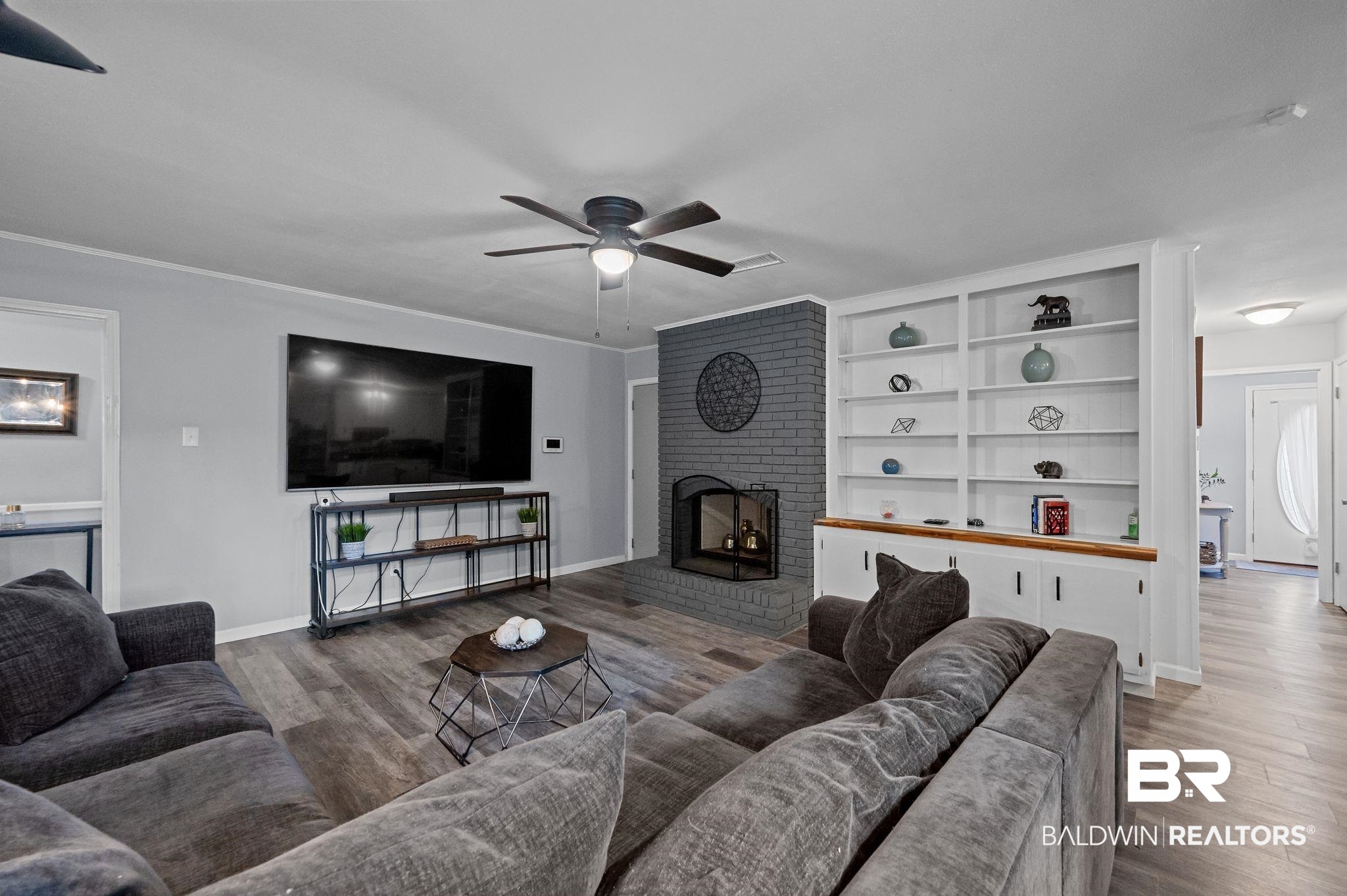 4724 Wicker Way Mobile, AL 36609 - Photo 15 of 36 Spacious living area featuring wood-finish flooring, a painted brick fireplace, and extensive built-in shelving with lower cabinetry