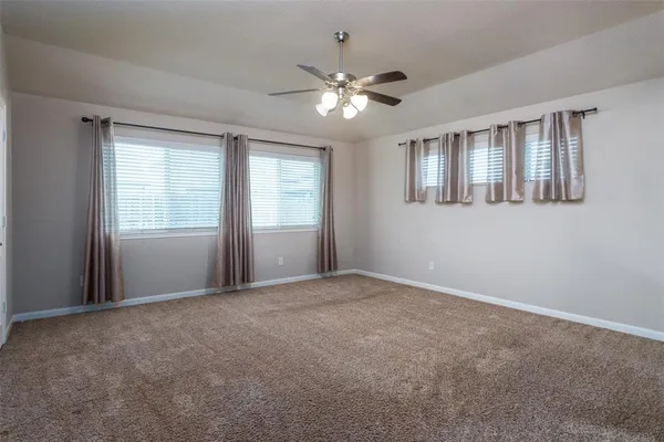 a view of an empty room with chandelier fan and windows