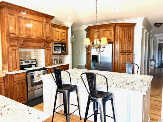 4310 Enoch Road Aynor, SC 29511 - Photo 12 of 39 Kitchen with brown cabinetry, a breakfast bar, hanging light fixtures, appliances with stainless steel finishes, and crown molding