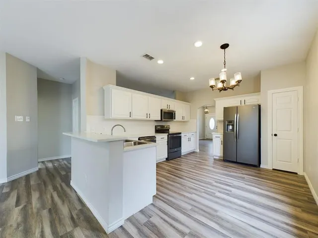 a kitchen with stainless steel appliances granite countertop a refrigerator a stove top oven a sink dishwasher and white cabinets with wooden floor