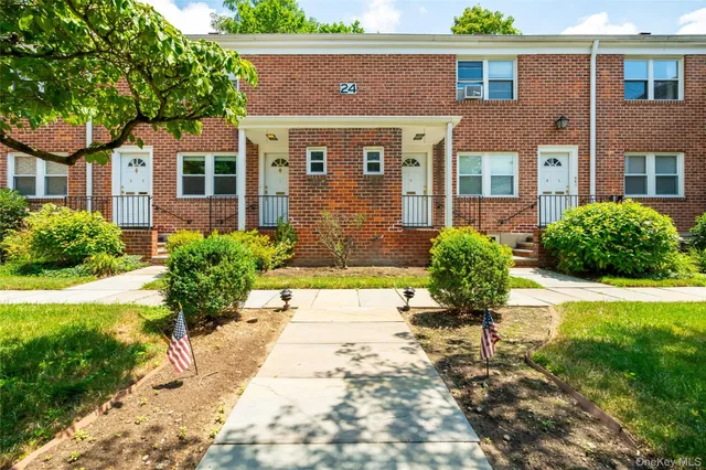 a view of a brick house with a yard plants and large tree