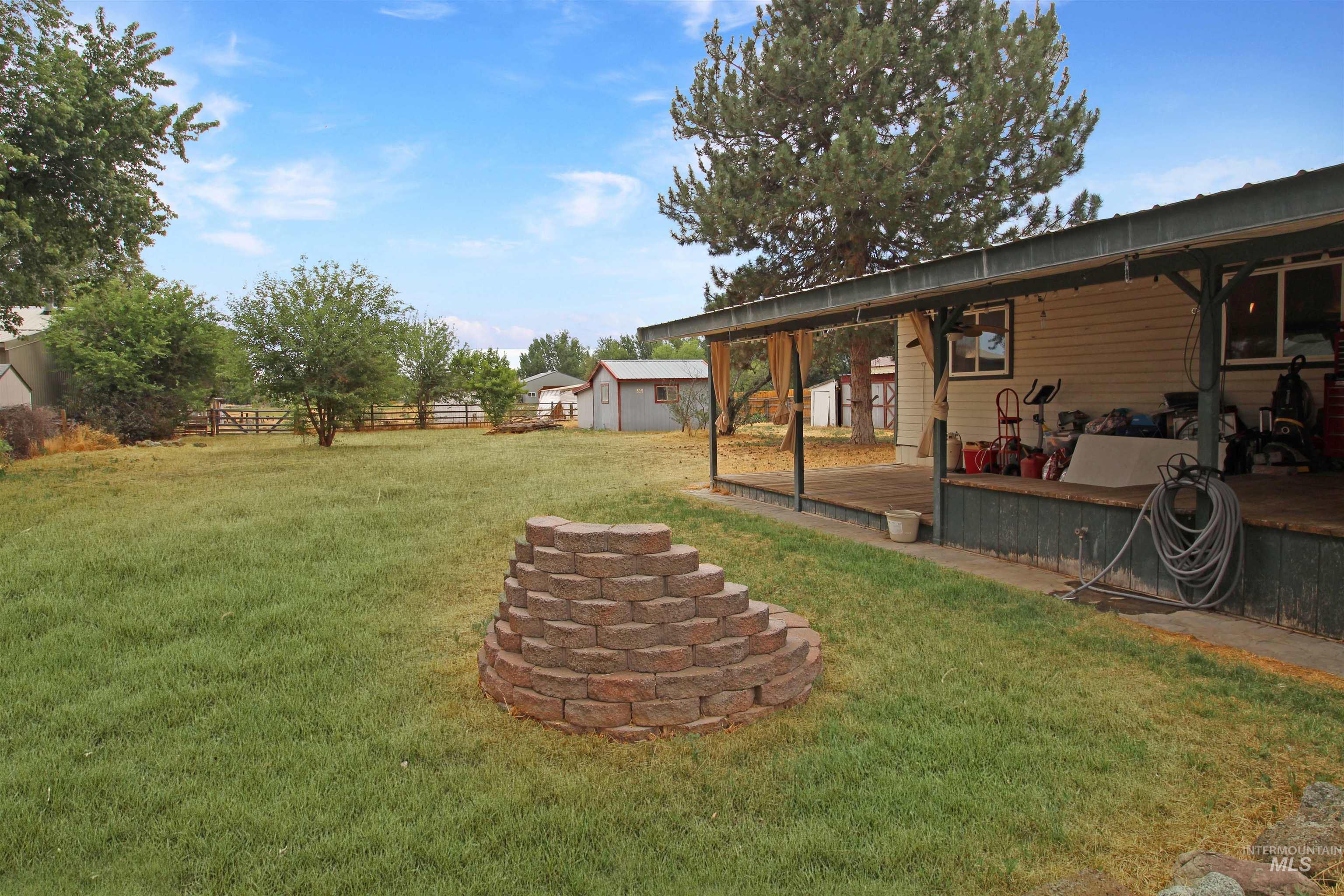 1265 Pioneer Road Weiser, ID 83672 - Photo 5 of 29 Expansive grassy yard featuring a stone block fire pit, a covered porch with wood flooring, and a metal roof