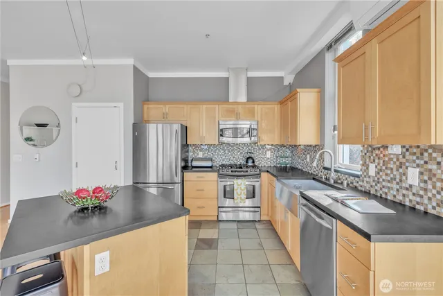 a living room with stainless steel appliances furniture a fireplace a flat screen tv and a kitchen view