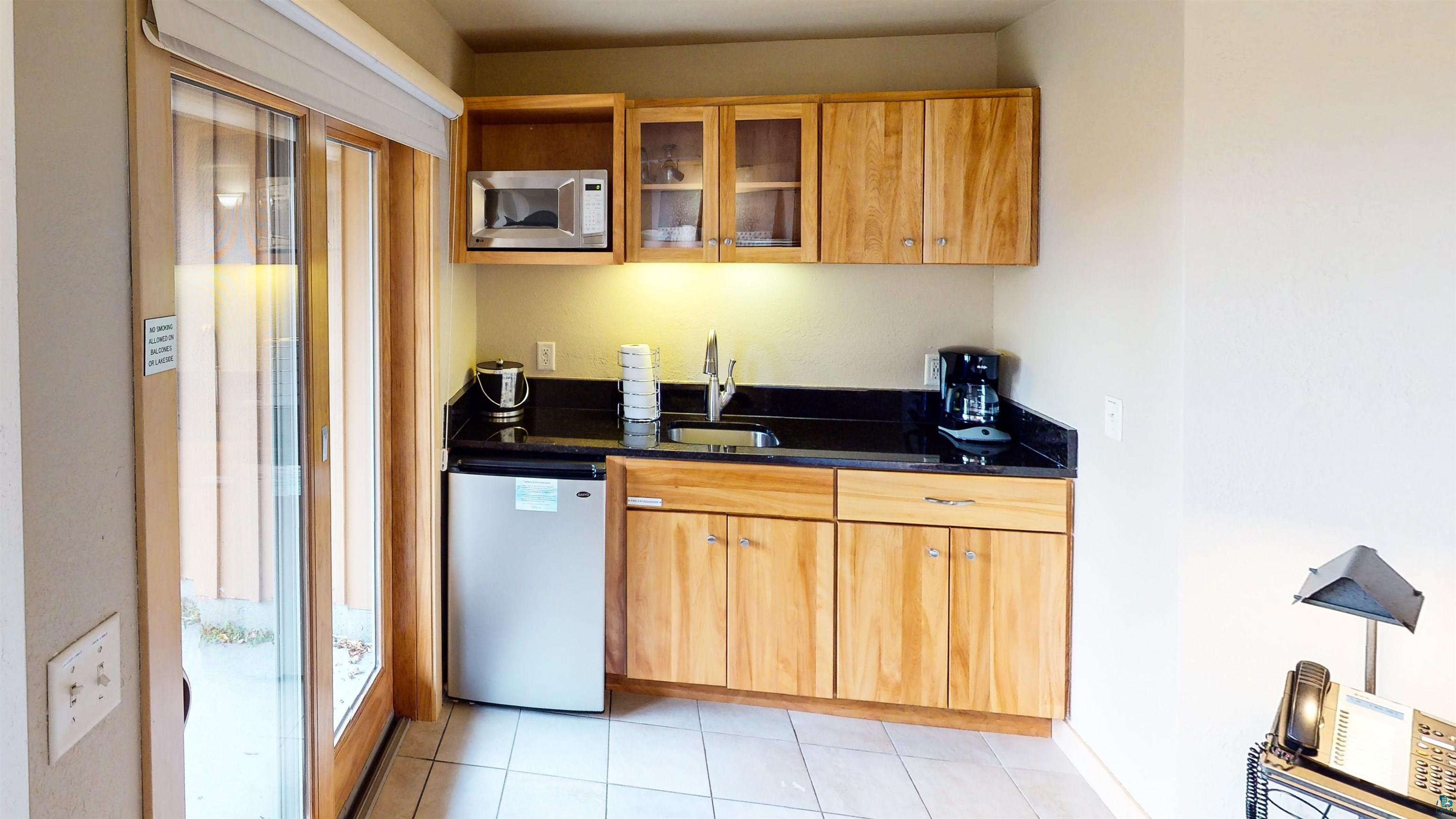 40 Surfside Drive, Unit 5D Tofte, MN 55615 - Photo 22 of 37 Kitchenette featuring wood cabinetry, stainless steel microwave, compact refrigerator, black countertop, and a stainless steel sink
