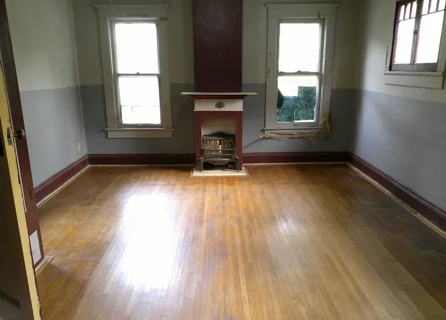 an empty room with wooden floor a fireplace and windows