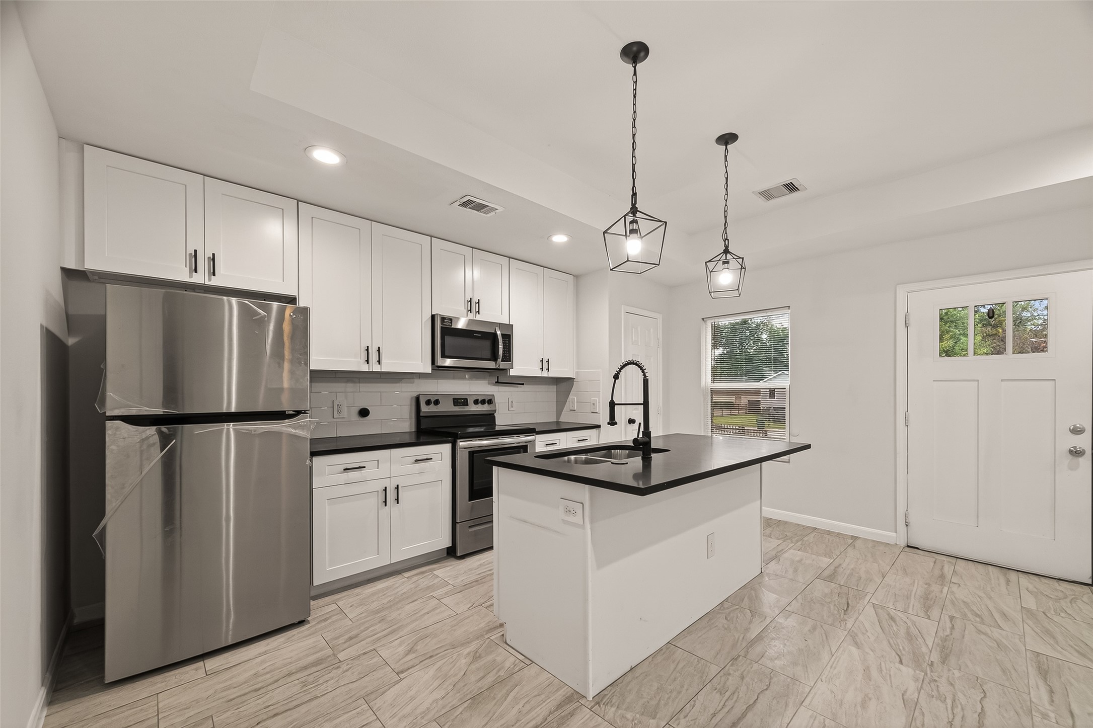 4302 Hirsch Road, Unit B Houston, TX 77026 - Photo 3 of 19 White cabinetry, and a contrasting black countertop island. Features pendant lighting, tiled flooring, and ample natural light from a nearby window and door.