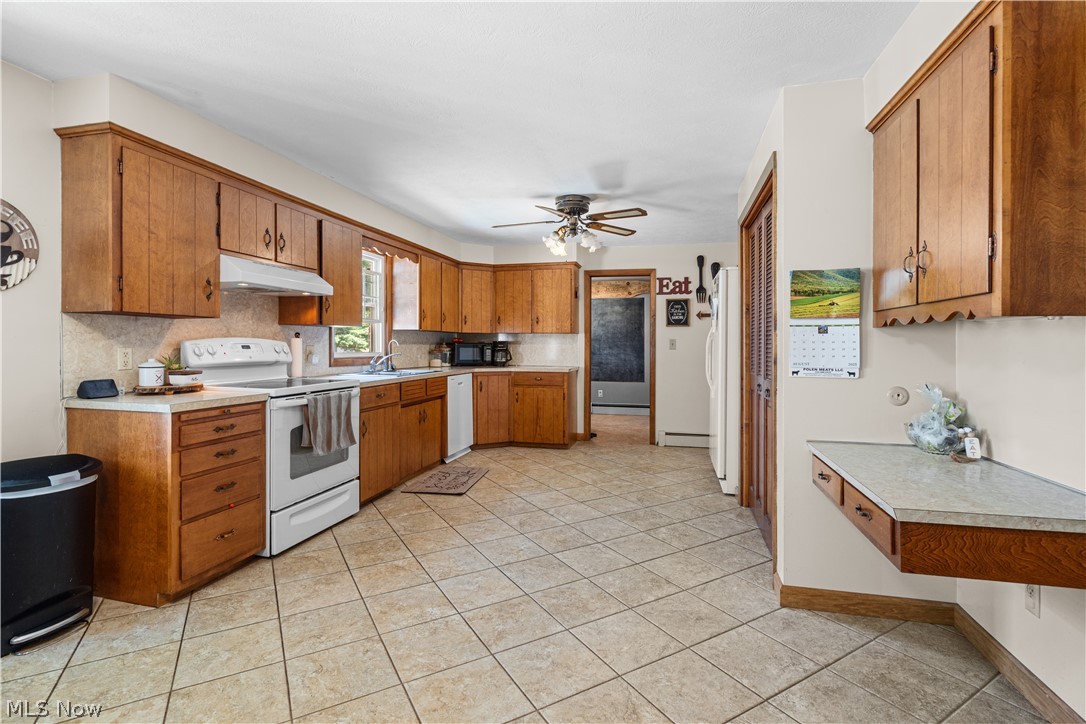 3650 Rambo Avenue Alliance, OH 44601 - Photo 13 of 36 Kitchen featuring extensive wood cabinetry, tile flooring, white appliances, a built-in desk area, and a ceiling fan