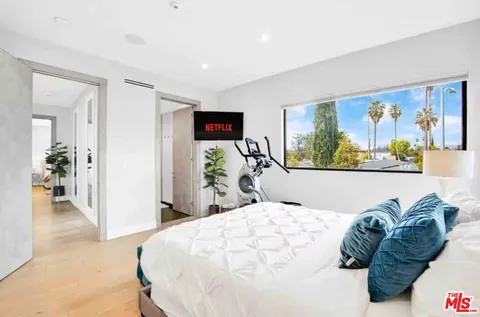 a bedroom with a bed painting and a large window