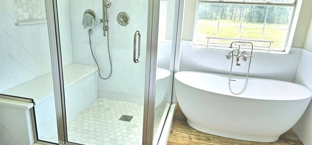 301 County Road Blossom, TX 75416 - Photo 13 of 19 Contemporary bathroom featuring a freestanding soaking tub with floor-mounted faucet, a glass-enclosed shower with a built-in bench, and white subway tile with a decorative accent band