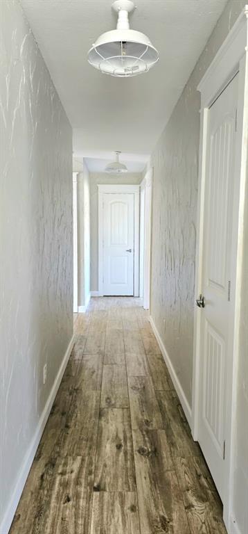 301 County Road Blossom, TX 75416 - Photo 15 of 19 Hallway featuring wood-finish flooring, white baseboards, textured walls, and industrial-style flush-mount lighting fixtures